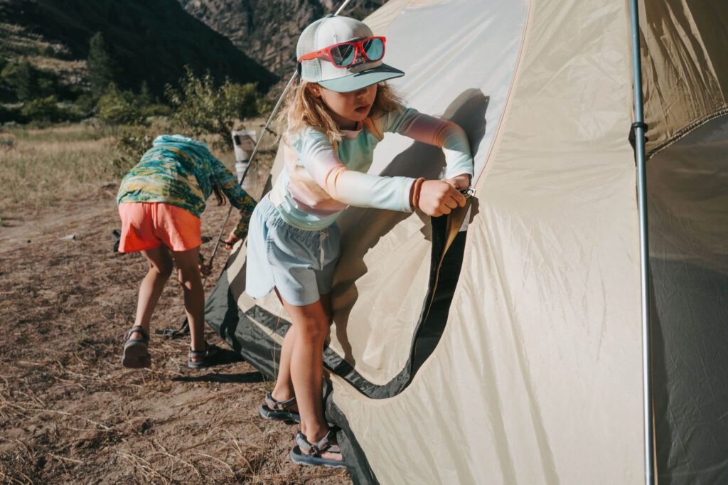 Two children zip a tent at a Middle Fork river camp