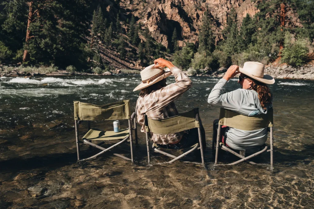 Two guests seated in camp chairs at the edge of the Middle Fork of the Salmon River